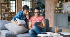 Jeune couple travaillant sur ordinateur tout en calculant ses finances assis sur le canapé